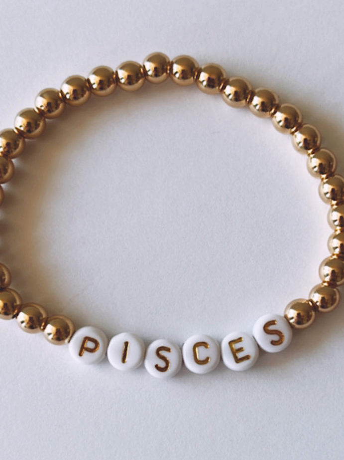 Gold and white beaded bracelet featuring the word "PISCES" on white beads.