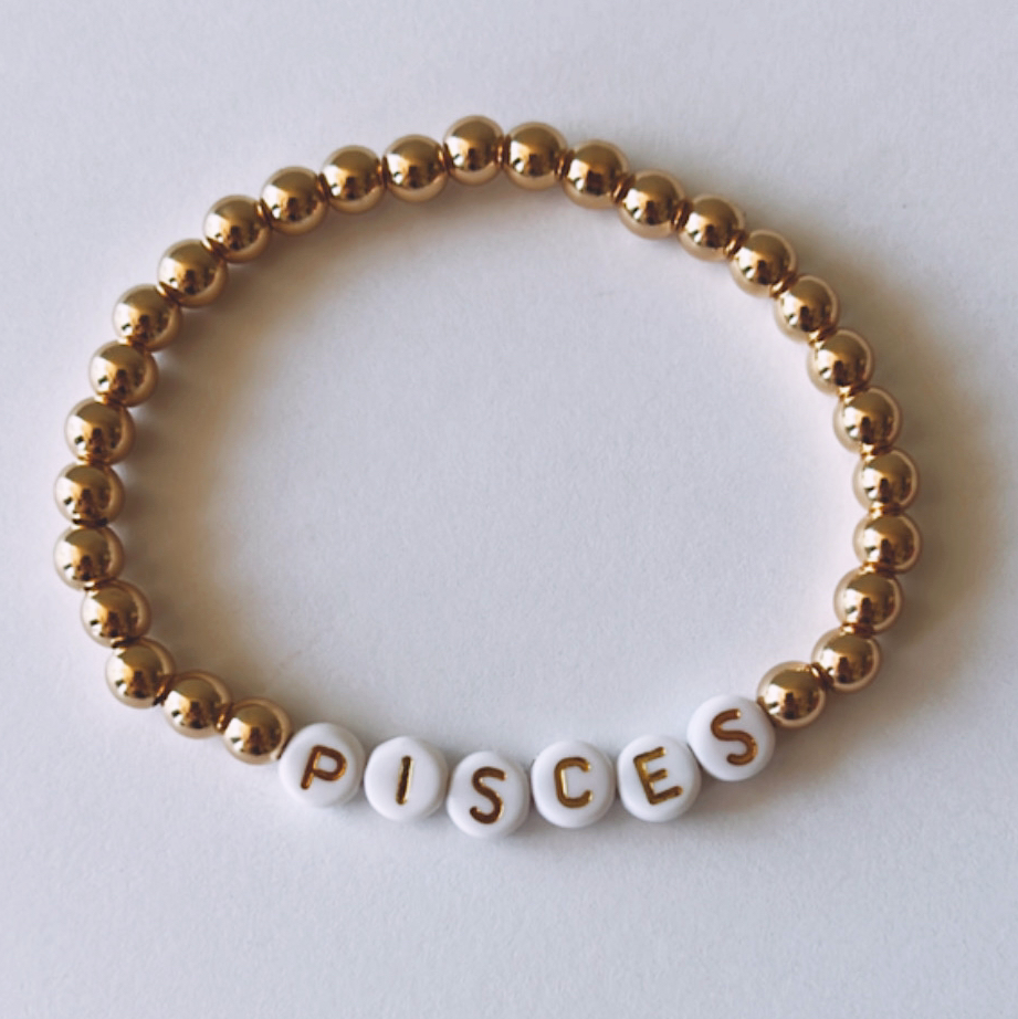 Gold and white beaded bracelet featuring the word "PISCES" on white beads.