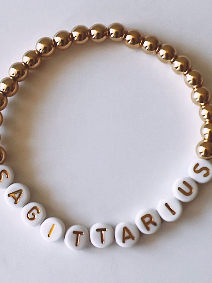 White and gold beaded bracelet featuring the word "SAGITTARIUS" spelled out in letter beads.