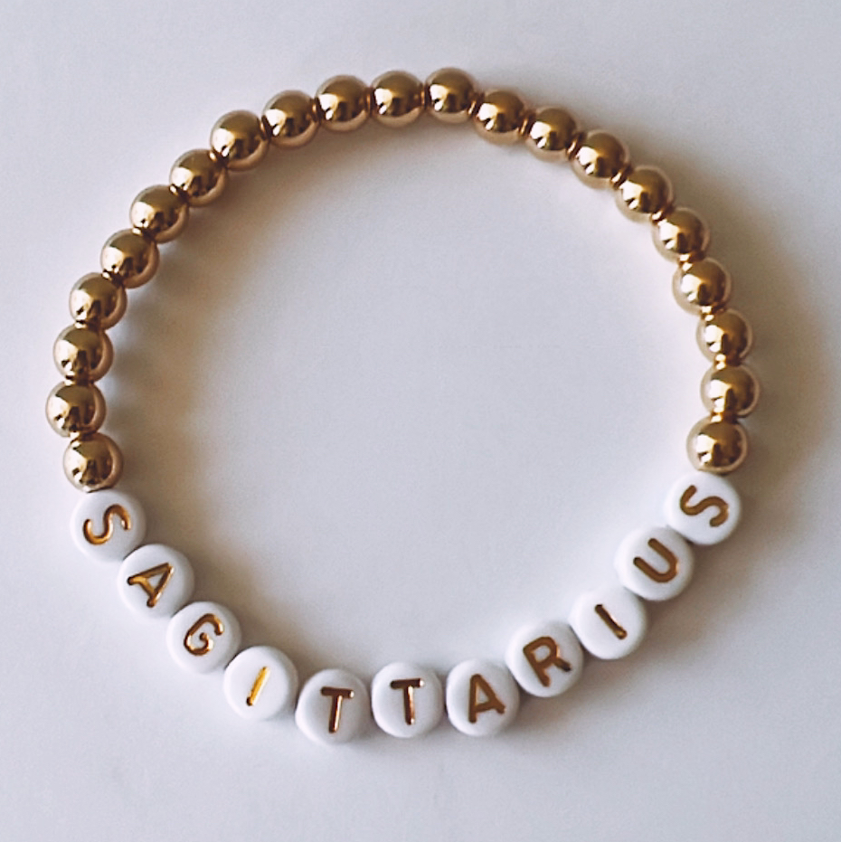 White and gold beaded bracelet featuring the word "SAGITTARIUS" spelled out in letter beads.