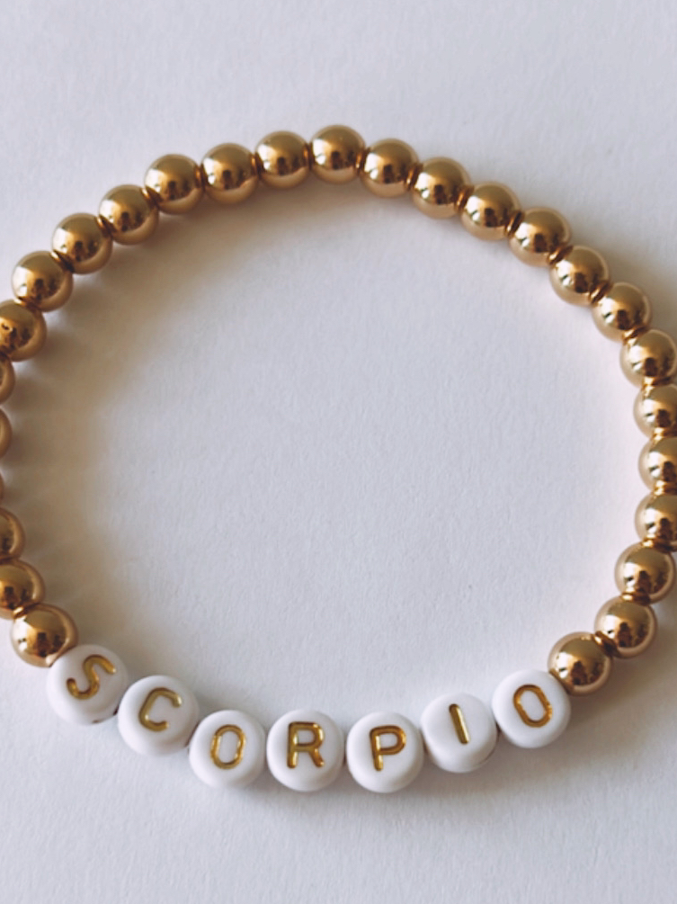Gold and white beaded bracelet featuring the word "SCORPIO" in block letters.