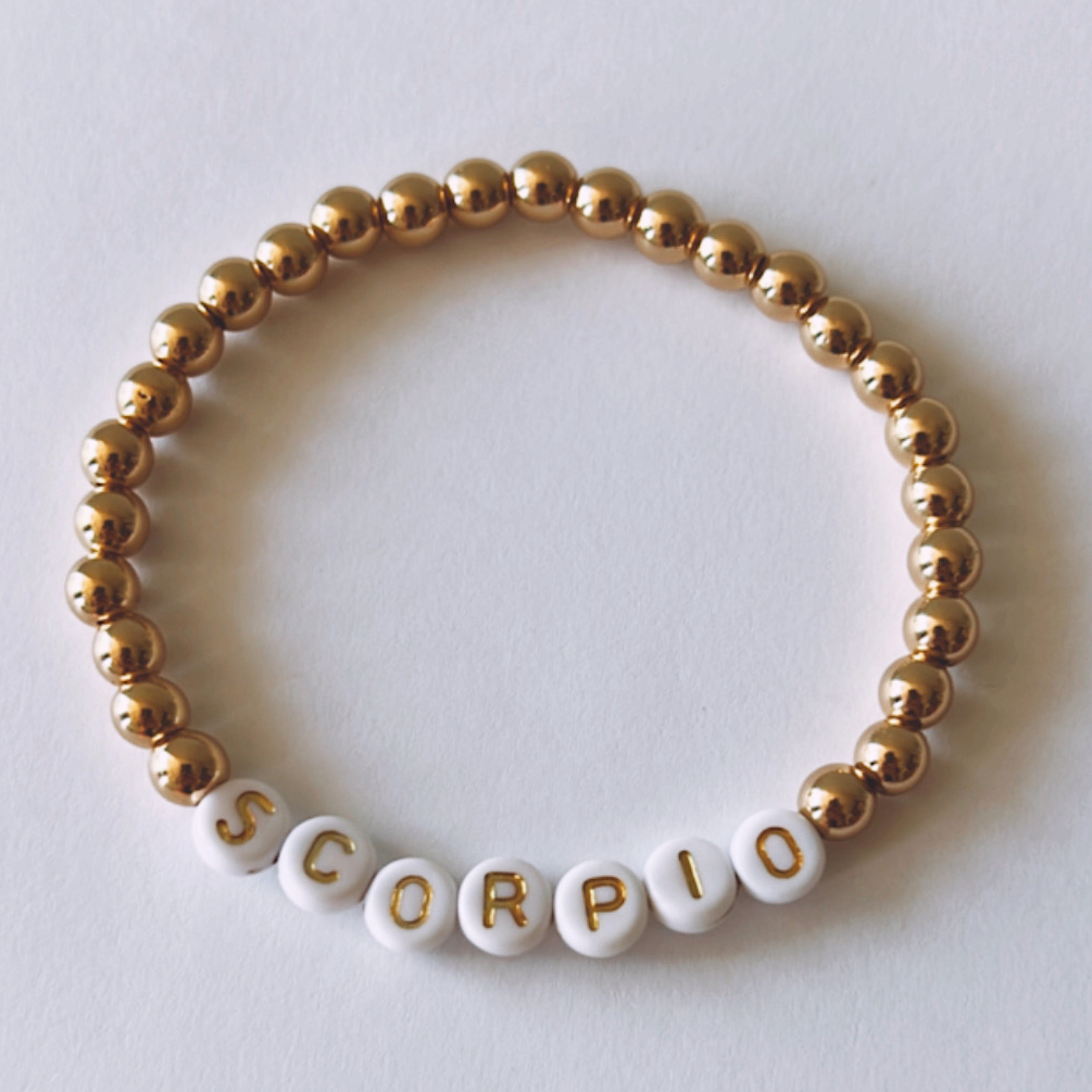 Gold and white beaded bracelet featuring the word "SCORPIO" in block letters.