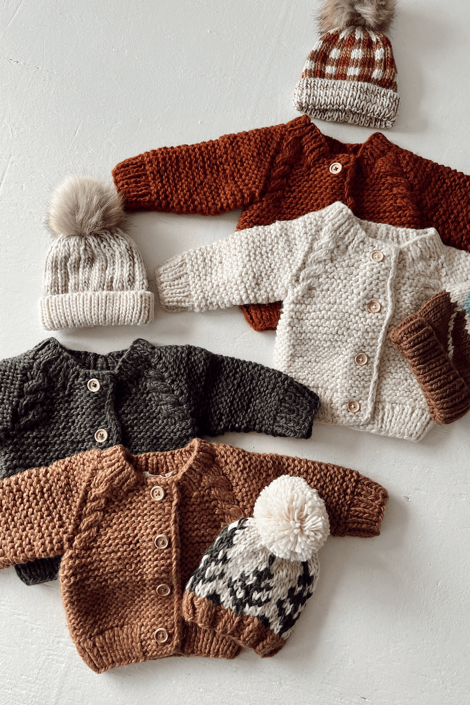 Knitted baby sweaters and hats in various colors, featuring buttons and playful pom-poms on top.