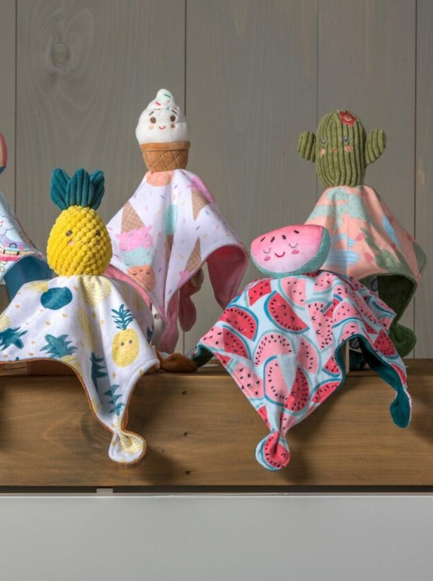 Colorful plush toys resembling fruit and ice cream, displayed on a wooden shelf against a light wall.