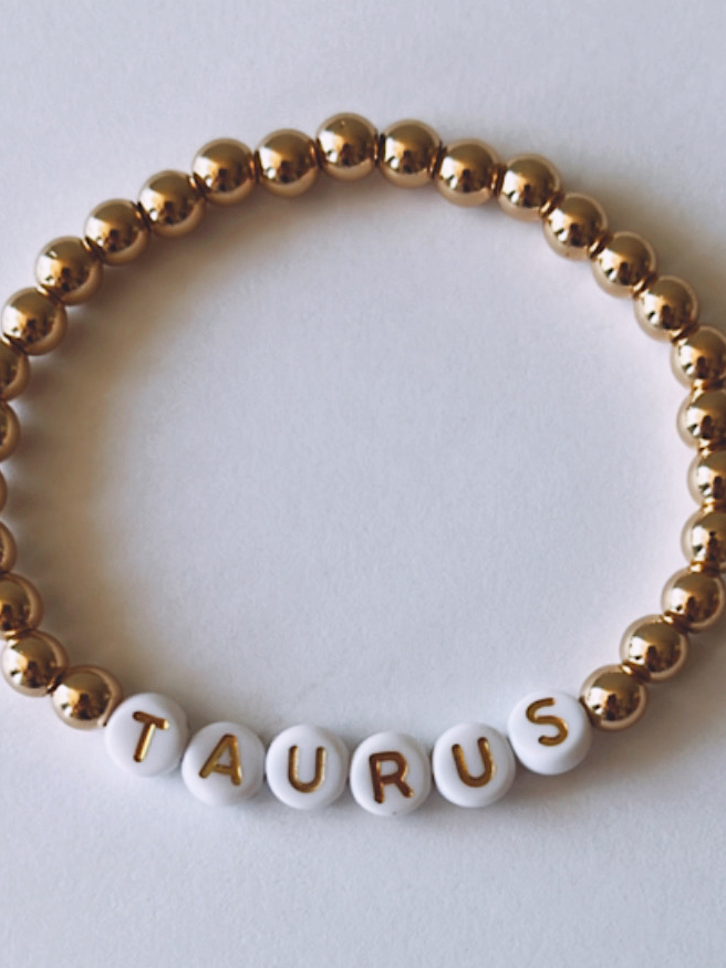 Gold and white beaded bracelet with the word "TAURUS" spelled out in letter beads.