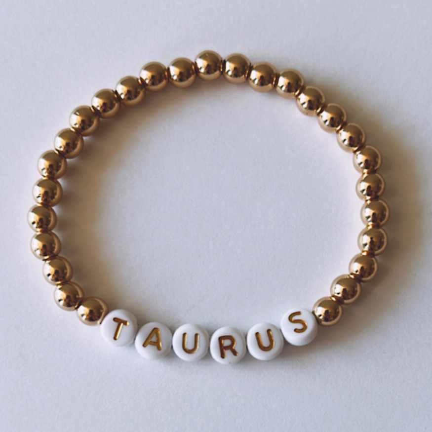 Gold and white beaded bracelet with the word "TAURUS" spelled out in letter beads.