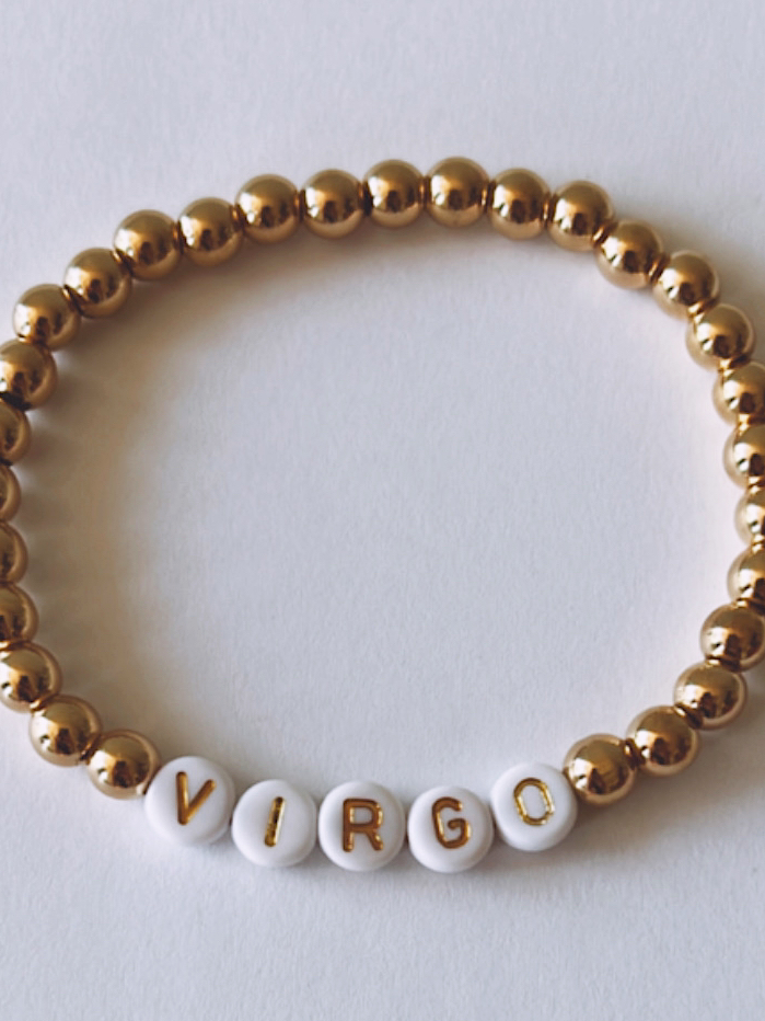 Gold and white beaded bracelet featuring the word "VIRGO" spelled out in letter beads.