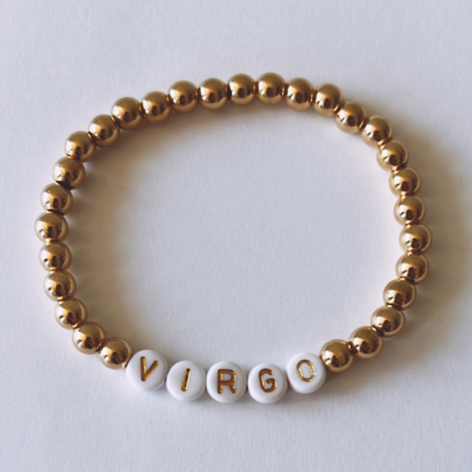 Gold and white beaded bracelet featuring the word "VIRGO" spelled out in letter beads.