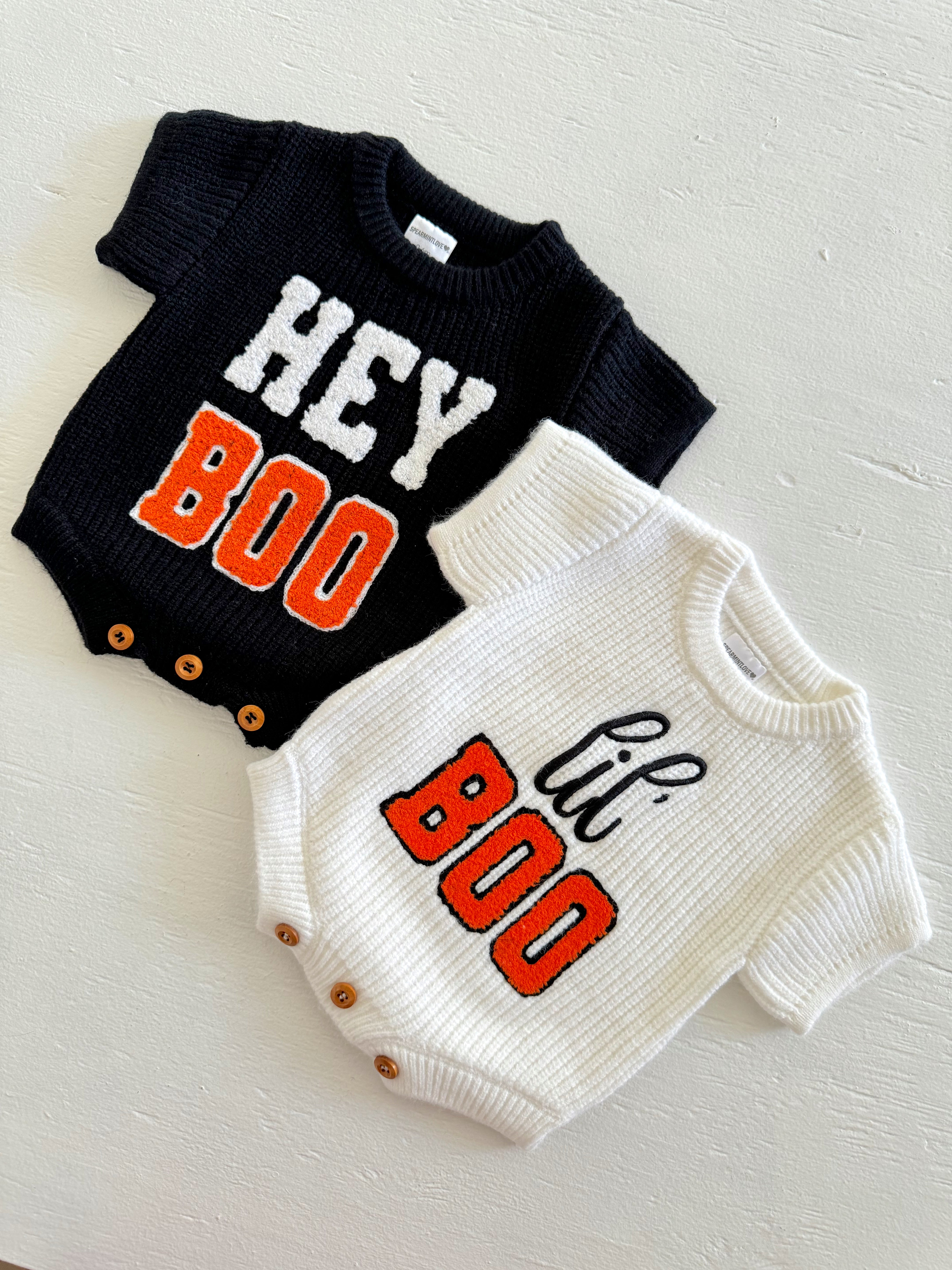 Black and white knitted baby bodysuits with "Hey Boo" and "lil' Boo" text in orange and black.