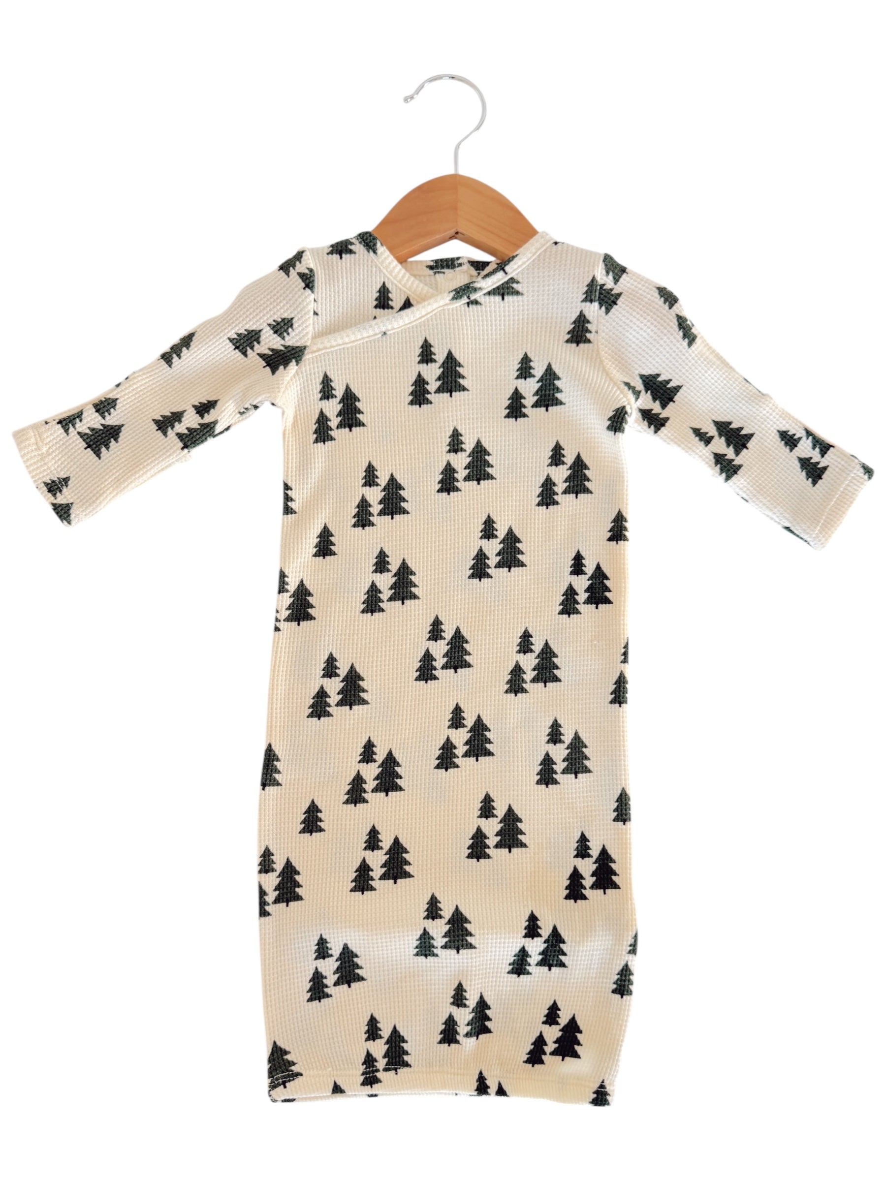 Long-sleeve baby outfit with a cream background and black tree patterns, hanging on a wooden hanger.