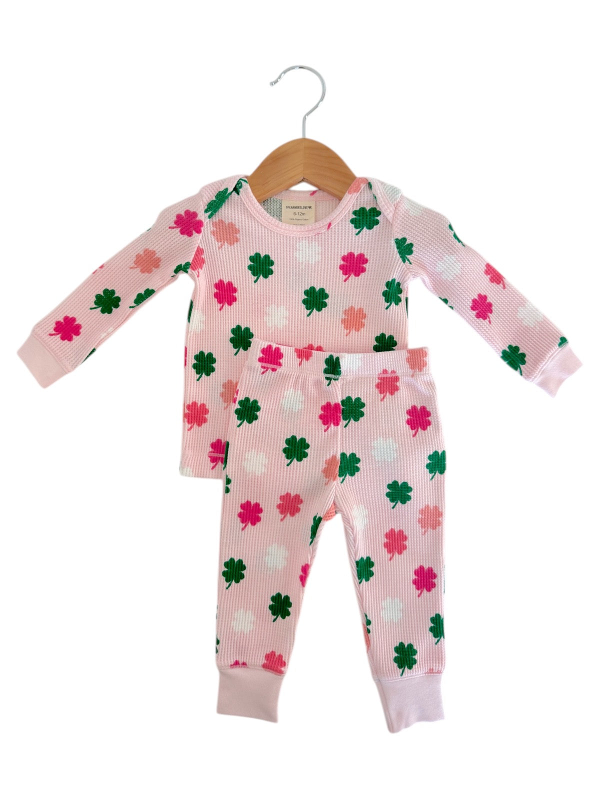 Pink children's pajamas with floral clover pattern, featuring long sleeves and matching pants, hanging on a wooden hanger.