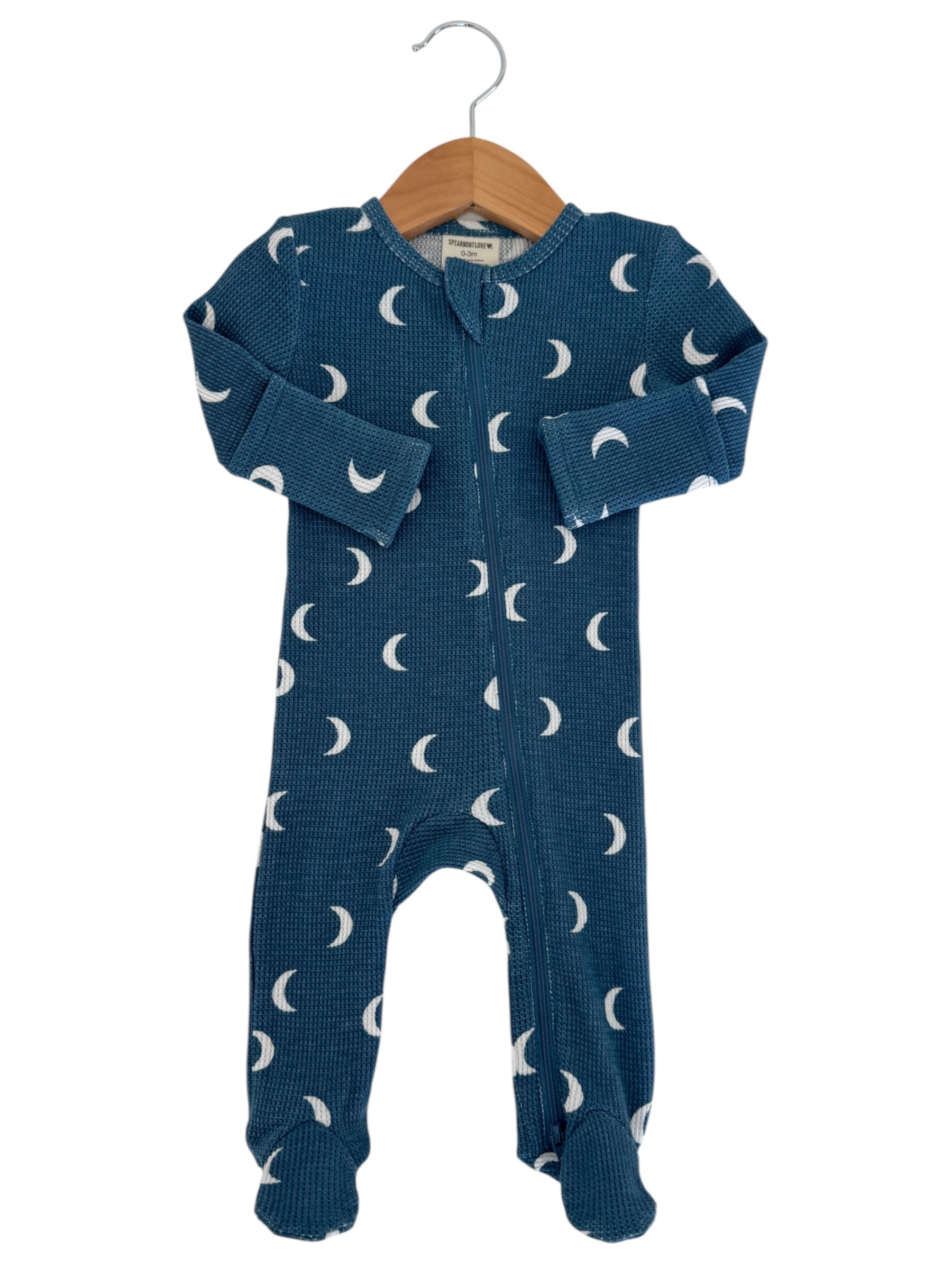 Blue baby onesie with white crescent moon patterns, hanging on a wooden hanger against a white background.