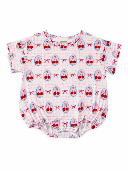 Pink baby onesie with a cherry and bow print, featuring short sleeves and a snap closure at the bottom.