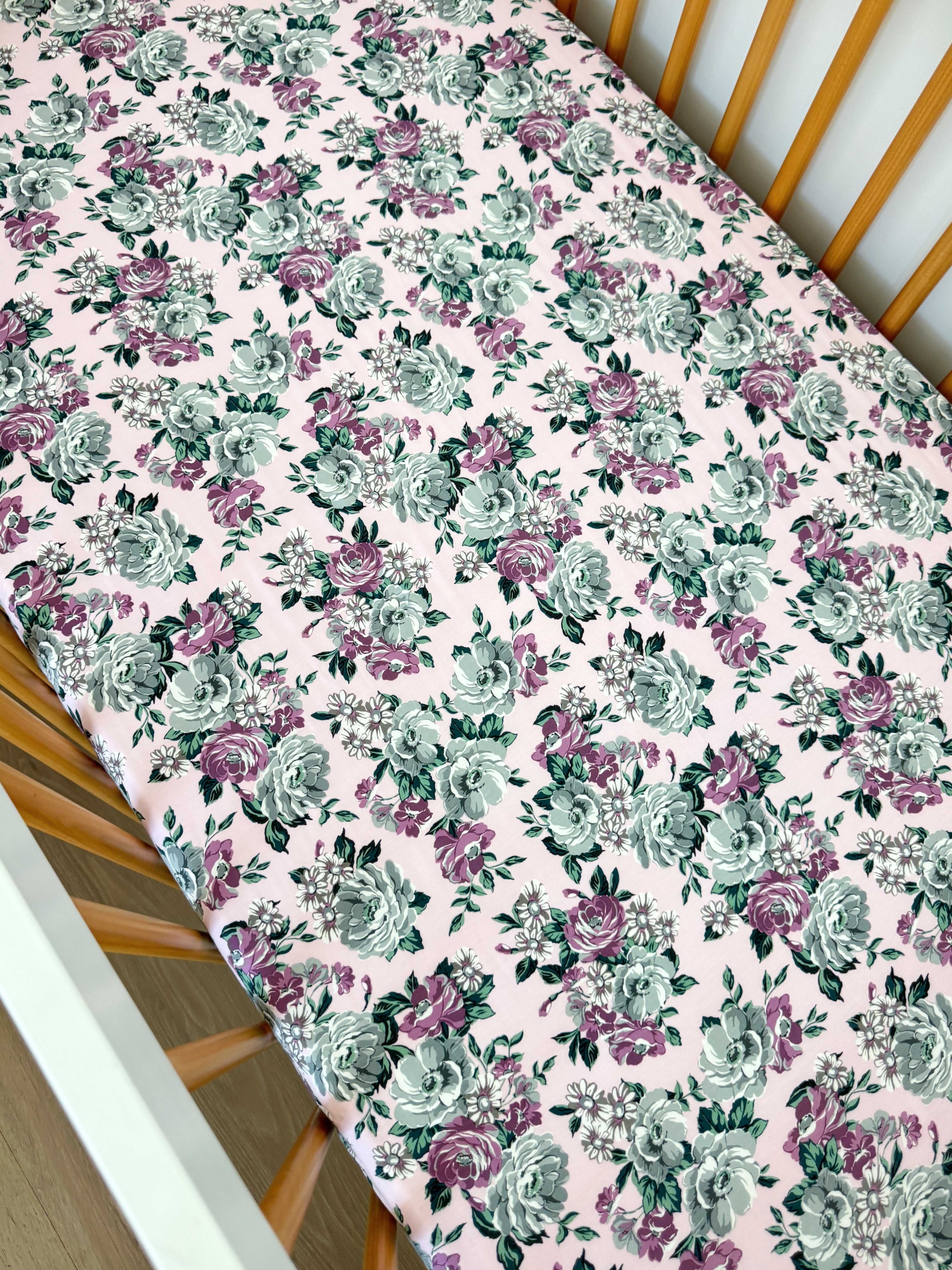 Floral-patterned crib sheet with pink background, featuring roses in green and purple hues.