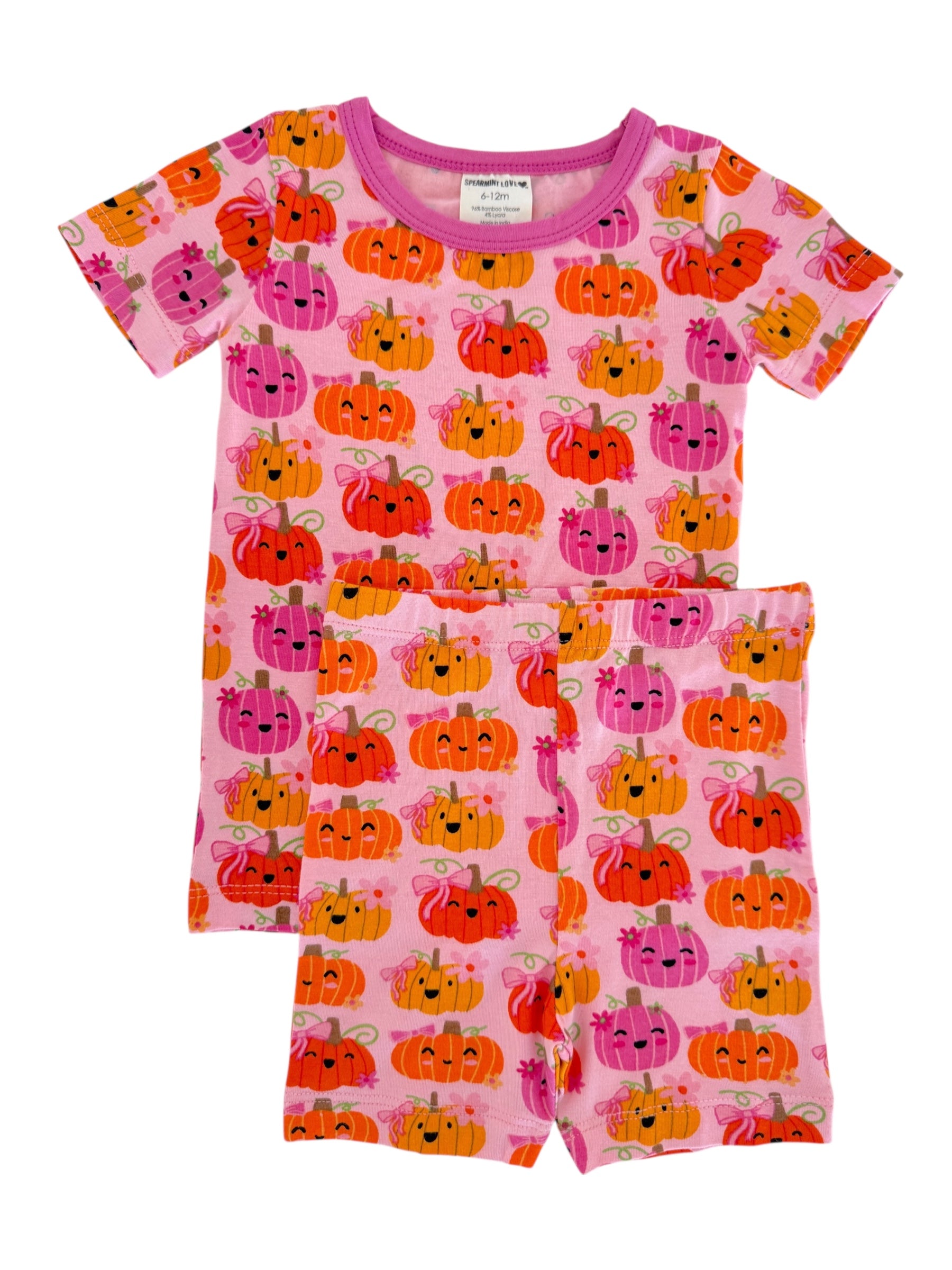 Kids' pajama set featuring a pink background with playful pumpkin patterns in orange, pink, and smiling faces.