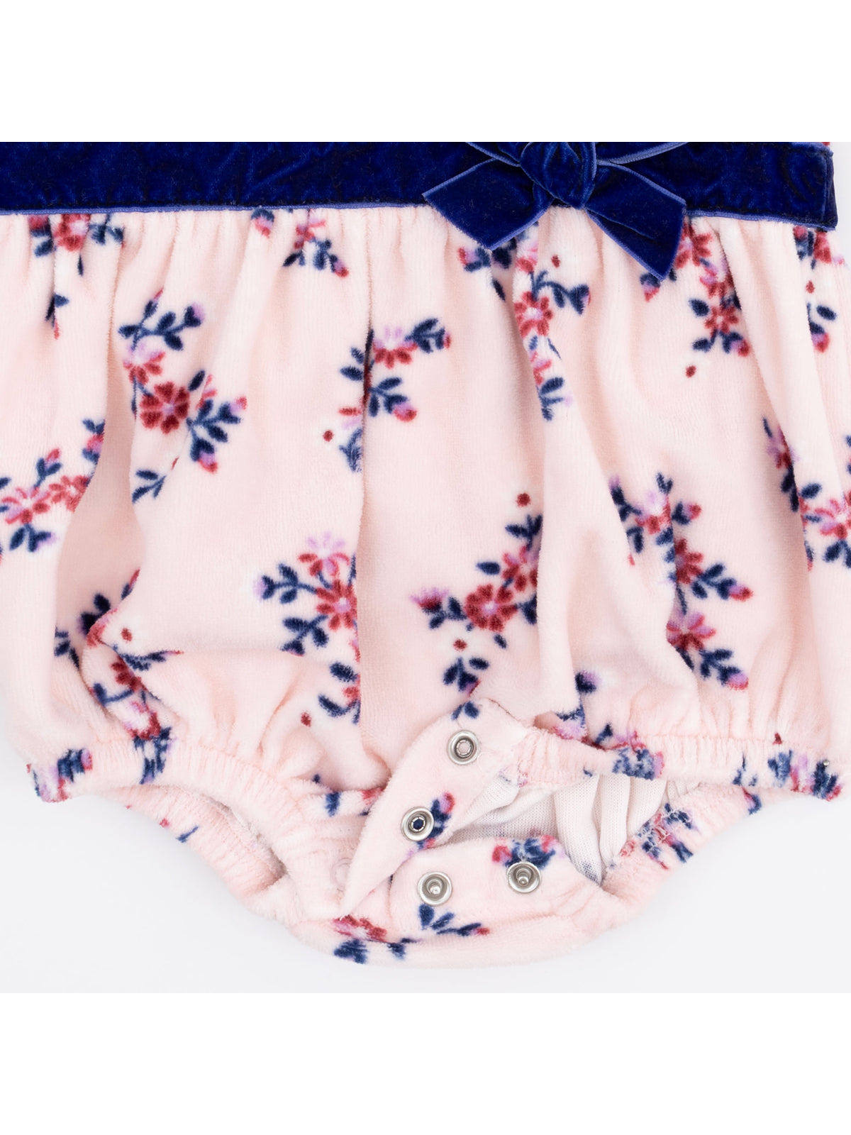 Floral baby romper in soft pink with navy velvet waistband and bow, featuring snap closures at the bottom.