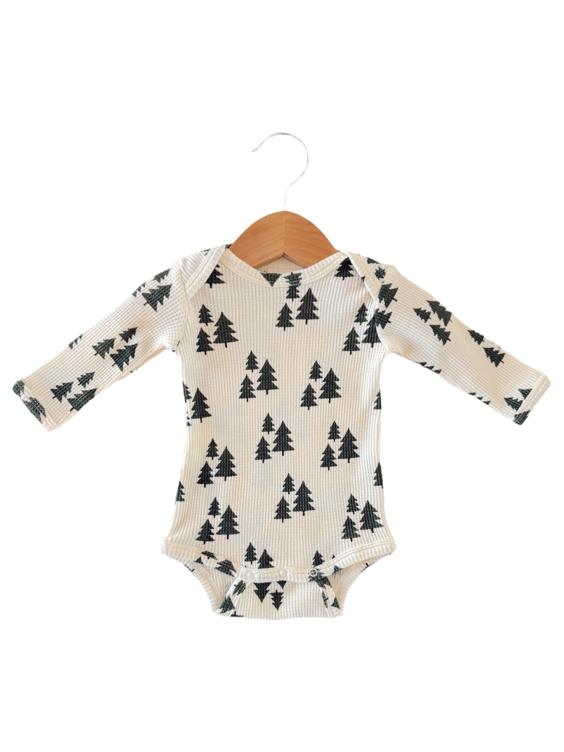 Cream-colored baby onesie with black tree pattern, displayed on a wooden hanger against a white background.