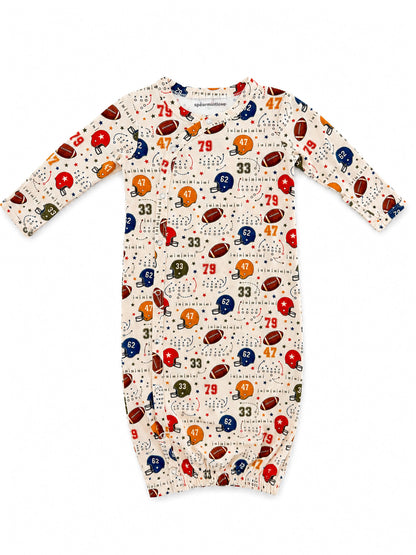 Infant football-themed sleeper with colorful helmet and ball prints on a cream background. Ideal for young sports fans.