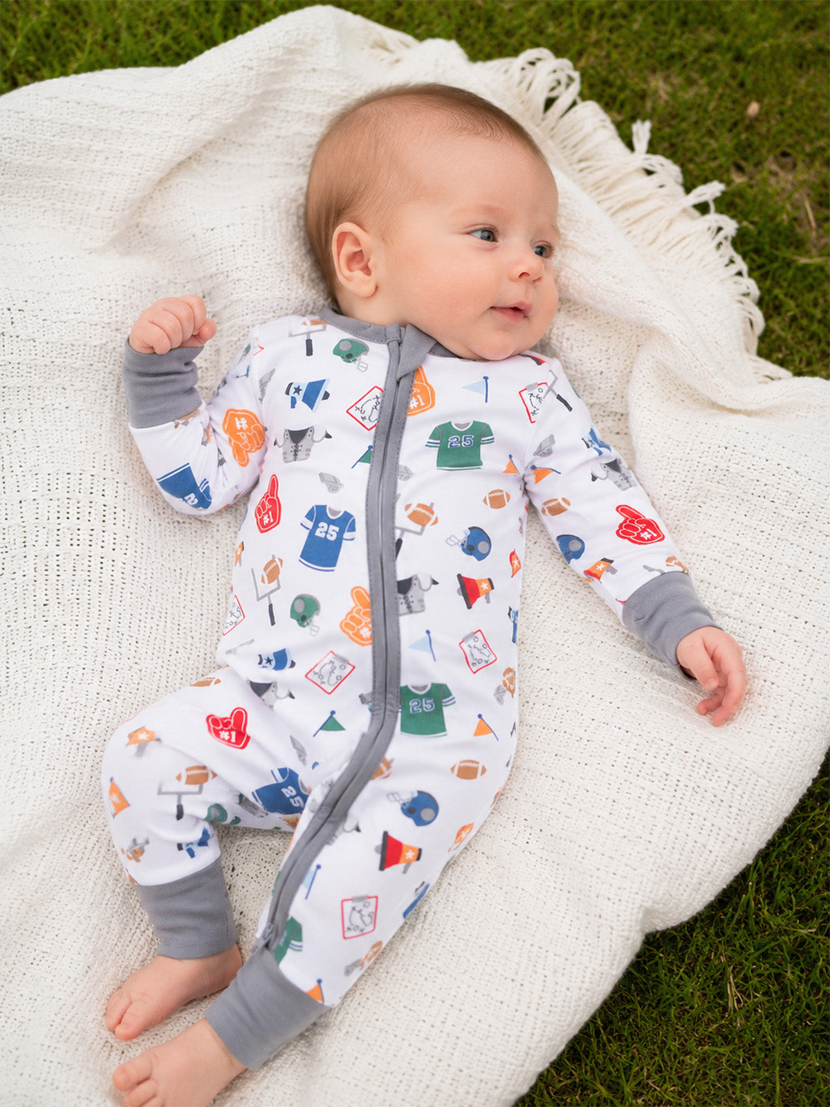 Baby in colorful sports-themed onesie laying on a soft blanket outdoors.