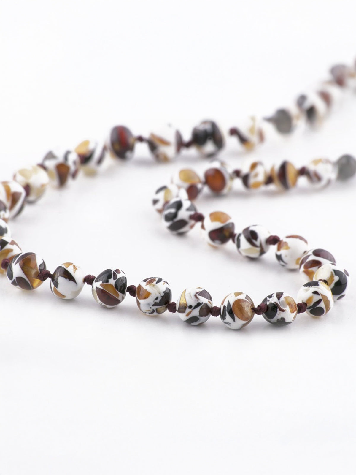 String of colorful, patterned beads in white, brown, and gold, lying flat on a light background.