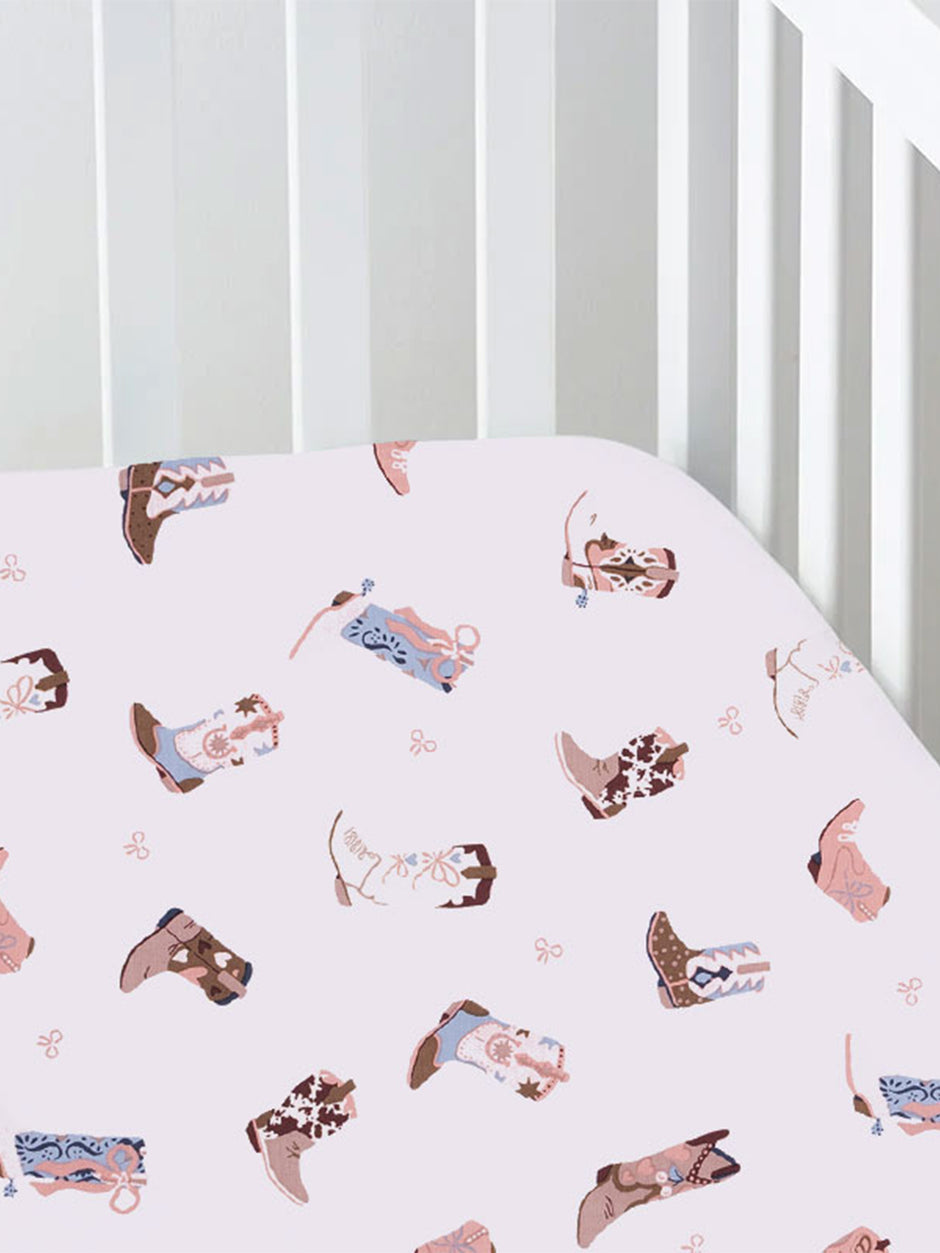 Cotton crib sheet with pink background and colorful cowboy boot patterns.