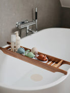 Wooden bath tray with soap, shampoo, and colorful dinosaur toys over a white tub.