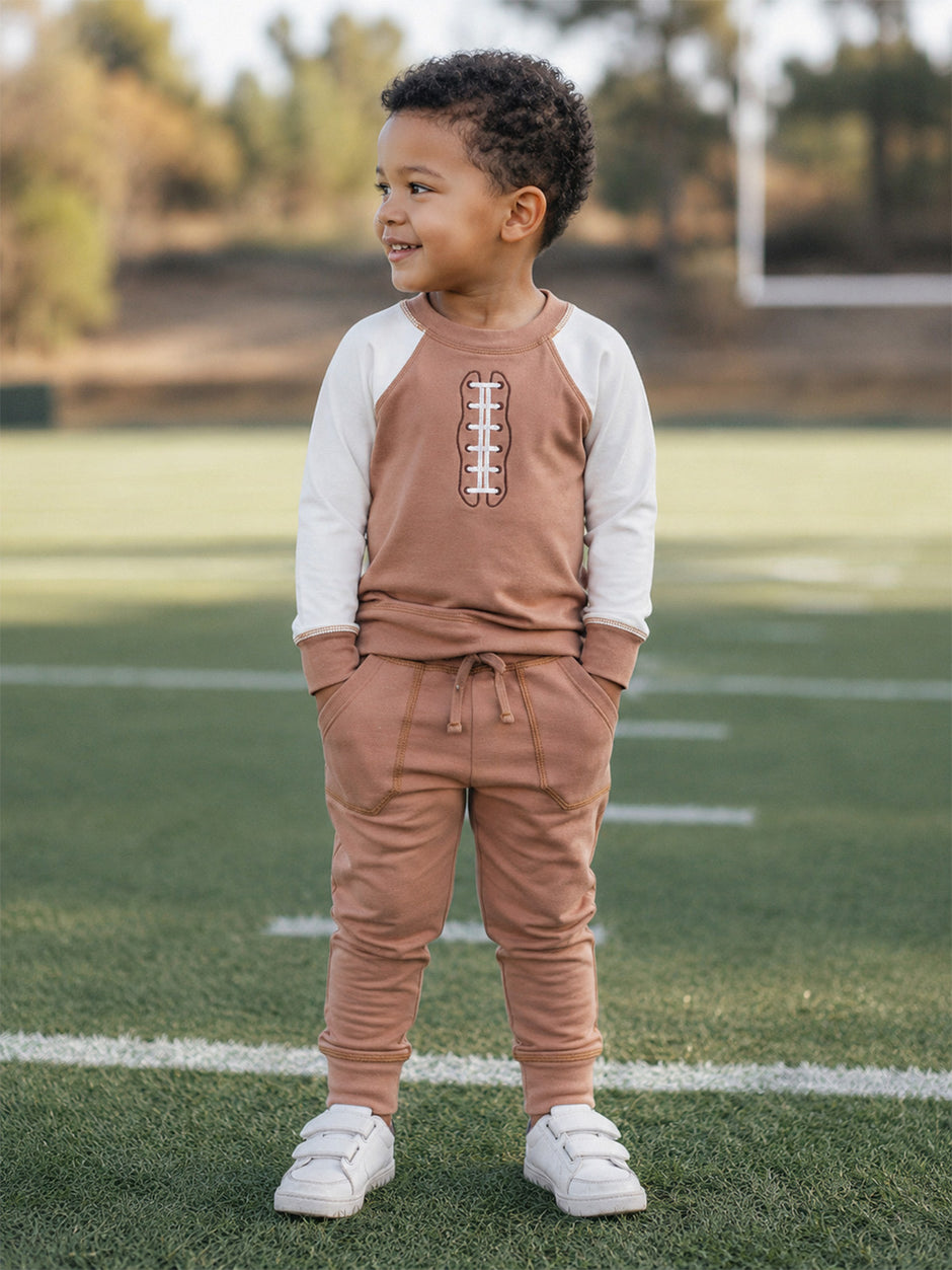 Smiling child in sporty outfit stands on a field, showcasing a playful, casual style with an athletic vibe.