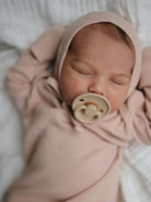 Sleeping baby in a light pink outfit and pacifier, resting on a textured white blanket.