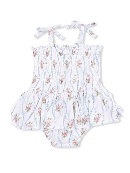 White floral baby romper with smocked bodice and tie straps, featuring a flared skirt and ruffled bottom.