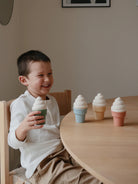 Boy laughing while holding a green ice cream cone, with three colorful cones on the table.