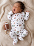 Infant yawning on a blanket, wearing a sports-themed onesie, with a toy football beside them.