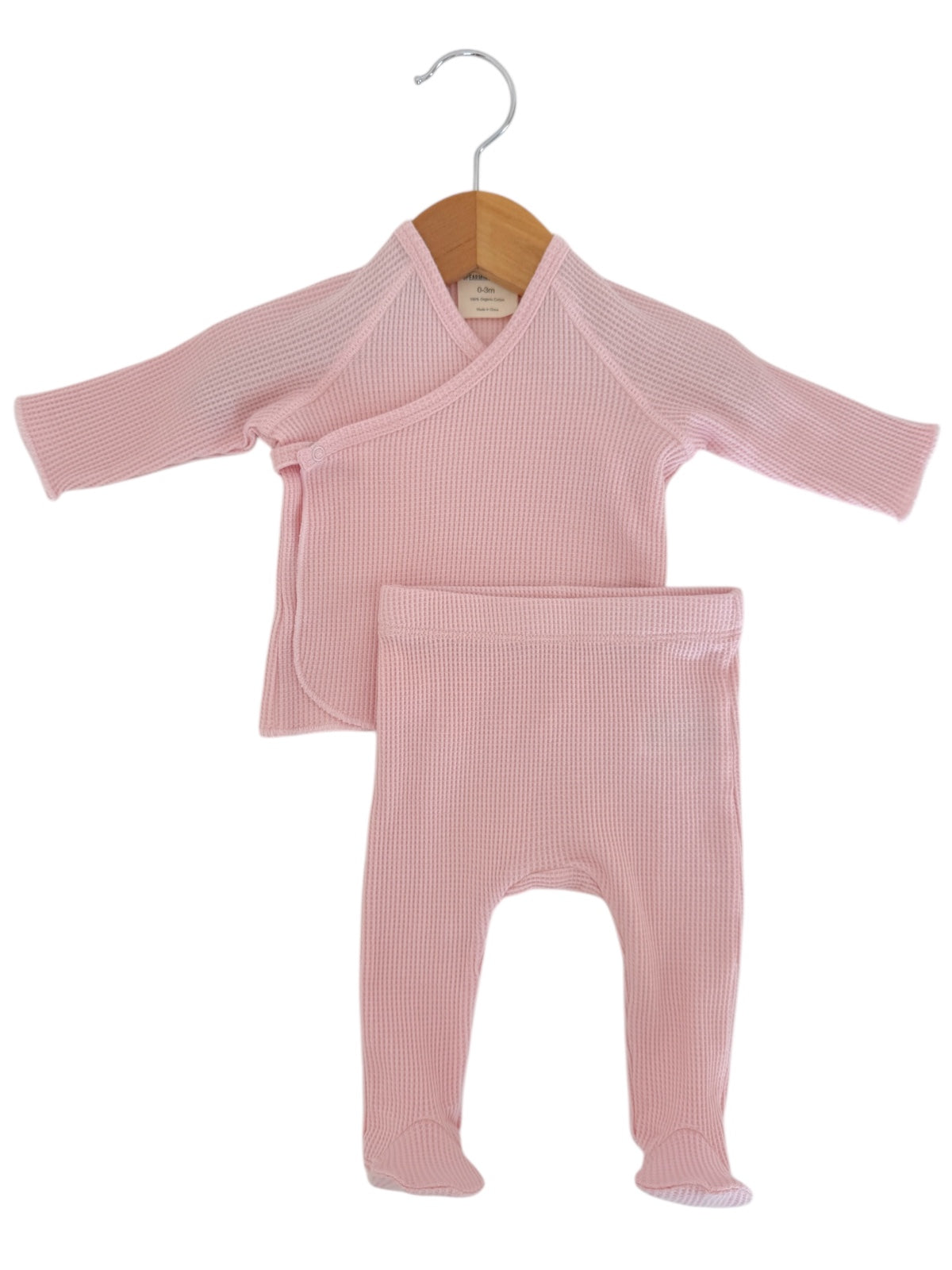 Pink infant outfit consisting of a long-sleeve wrap top and matching pants hanging on a wooden hanger.