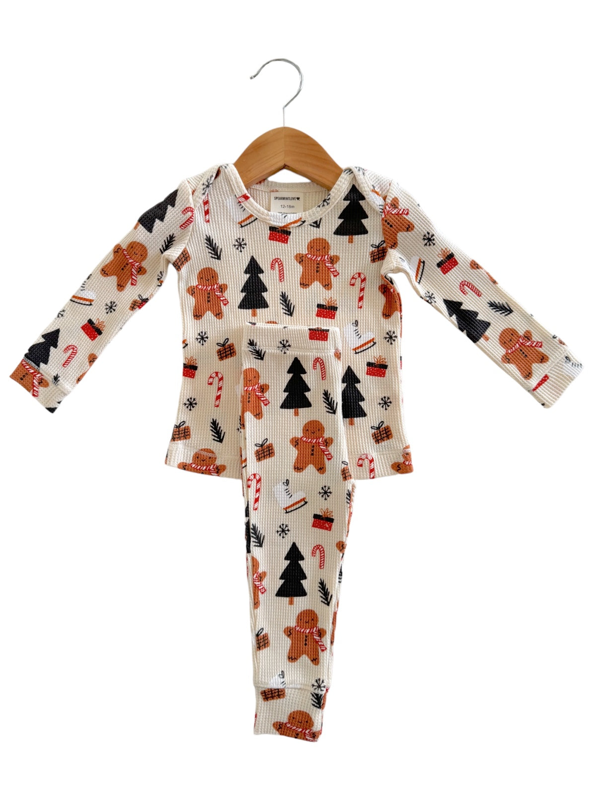 Child's holiday pajamas featuring gingerbread men, candy canes, and Christmas trees on a cream background.