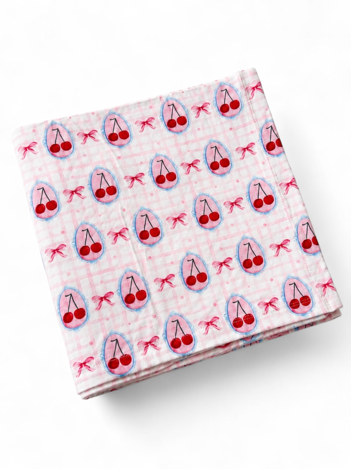 Pink fabric with a cherry pattern, featuring small red cherries and bows on a checked background.