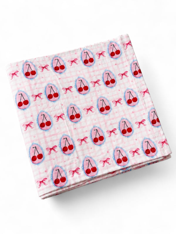 Pink fabric with a cherry pattern, featuring small red cherries and bows on a checked background.