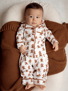 Baby in gingerbread-themed pajamas resting on a cozy brown blanket, with a calm expression.