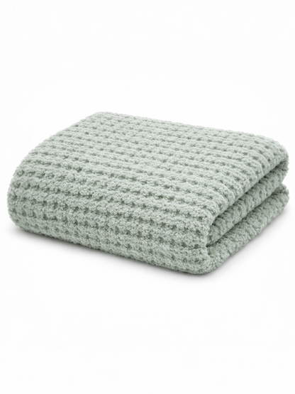 Soft green blanket with a textured, woven pattern, neatly folded on a light background.
