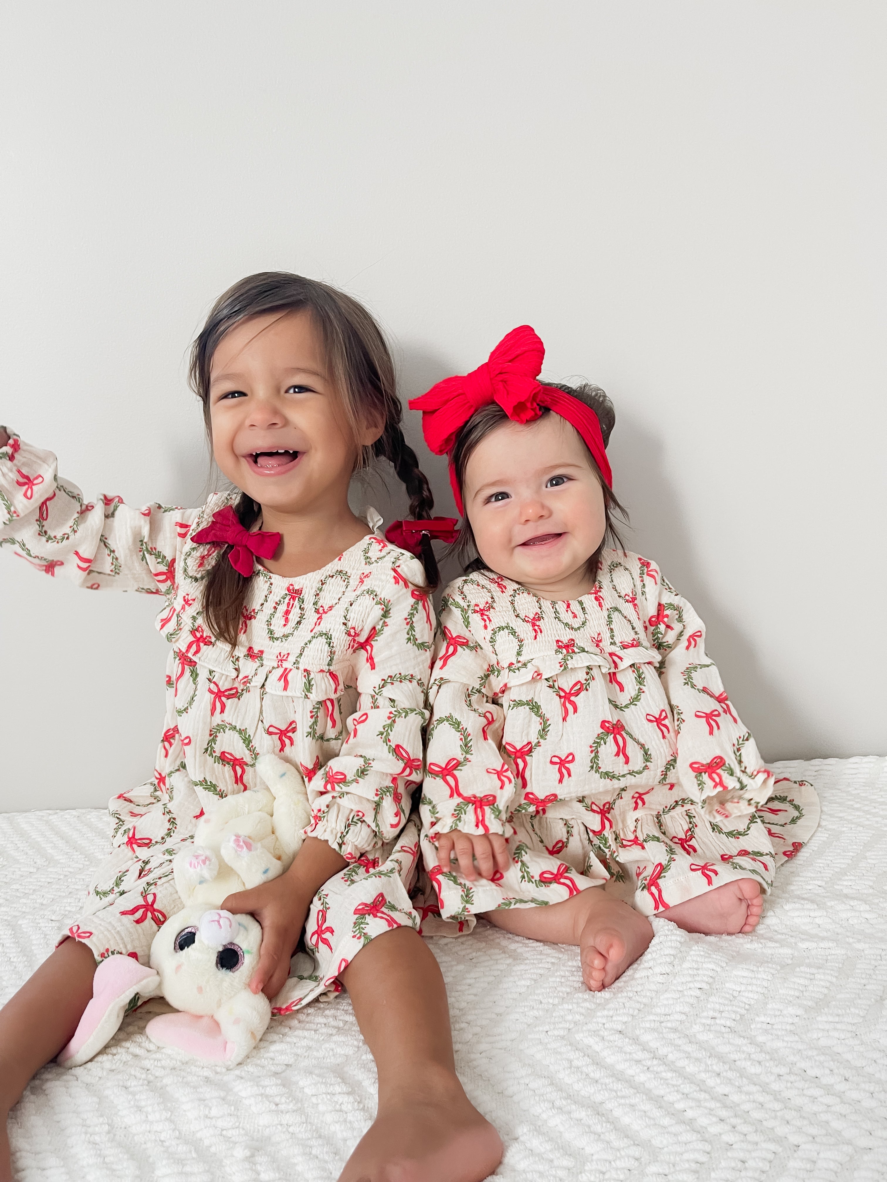 Two smiling young girls in matching holiday dresses, one holding a bunny toy, against a white background.
