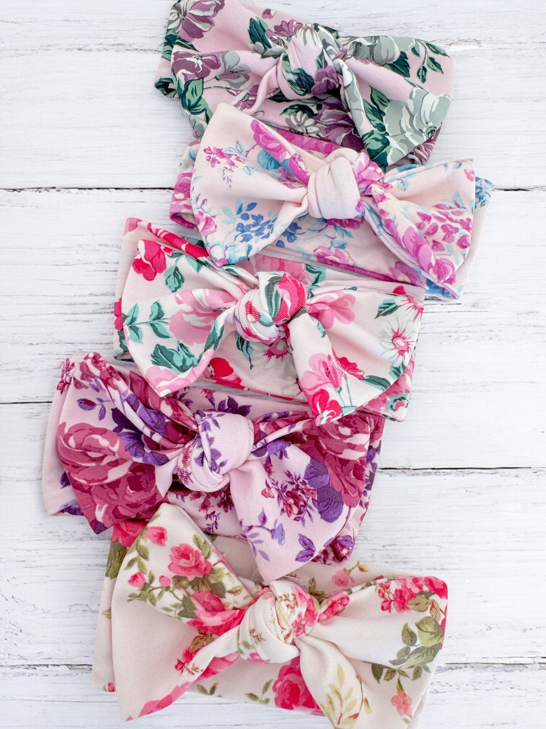 Five floral-patterned fabric bows arranged neatly on a wooden background.