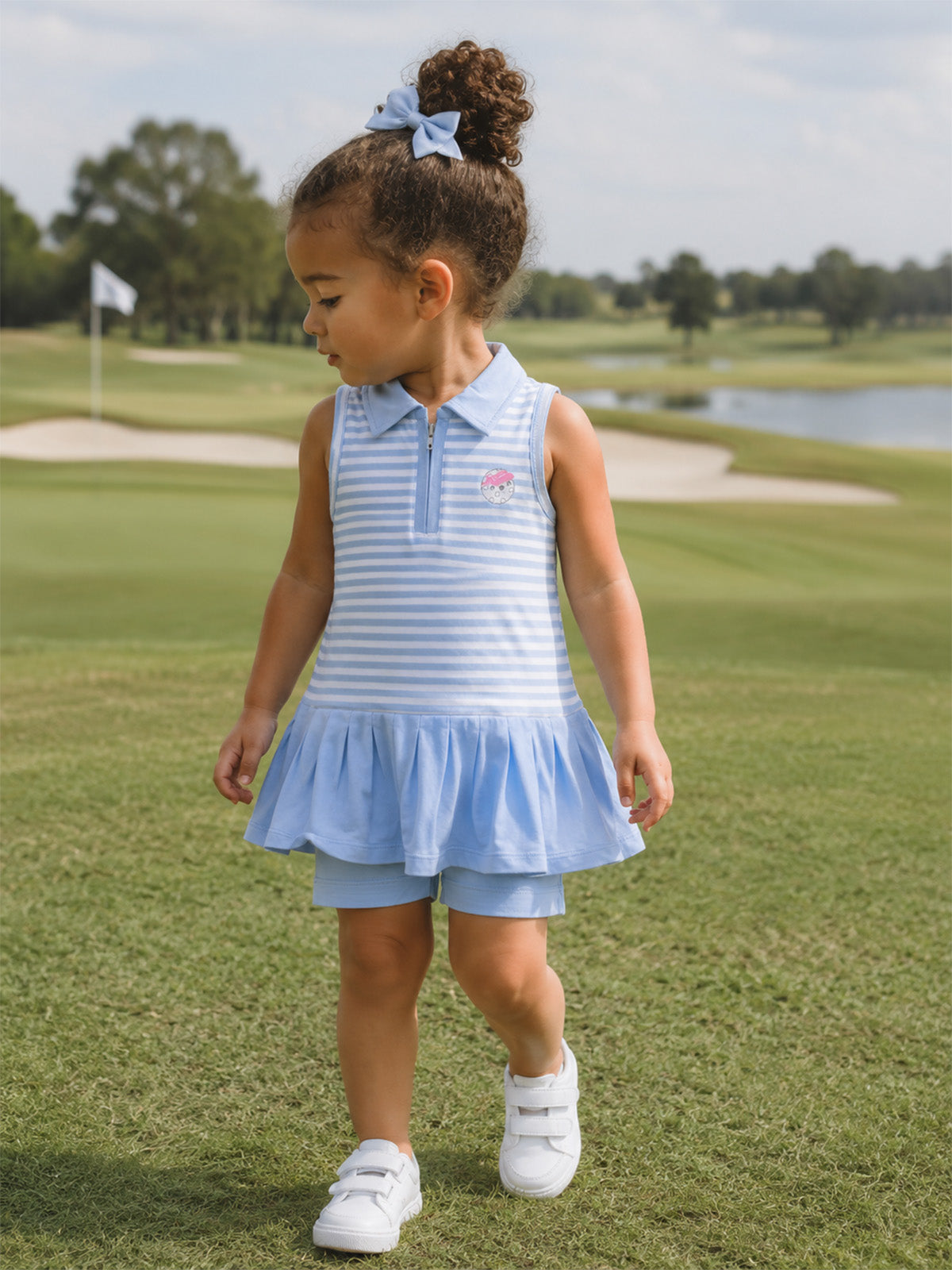 A young girl in a blue striped dress with a flared skirt, walking on a golf course.