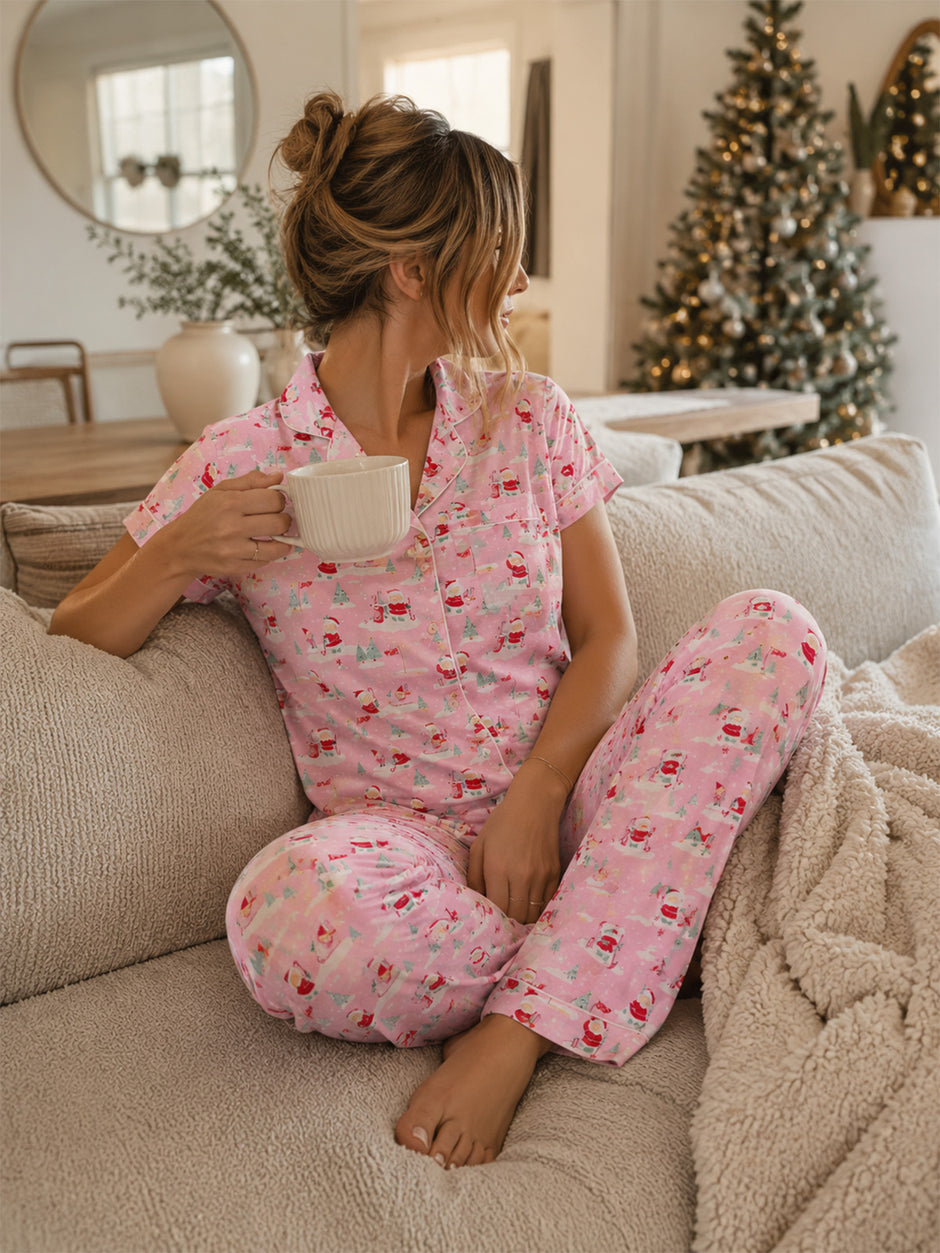 Woman in festive pajamas sitting on a couch, holding a mug, with a Christmas tree in the background.