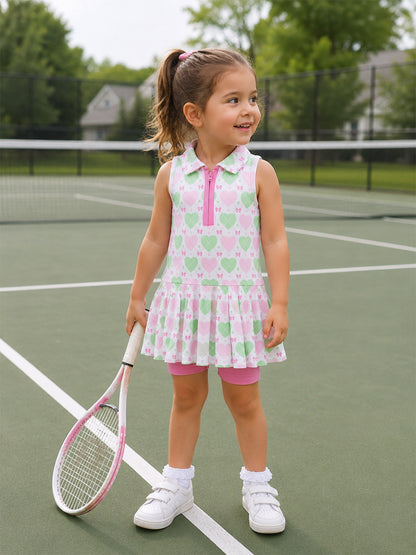 Smiling girl in a colorful tennis outfit stands on a court, holding a racket, ready to play.