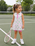 Smiling girl in a colorful tennis outfit stands on a court, holding a racket, ready to play.
