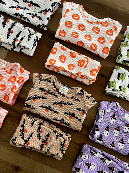 Colorful Halloween-themed children's clothing stacked on a wooden surface, featuring pumpkins, bats, and ghosts.