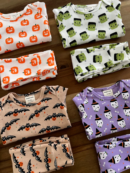 Colorful, folded Halloween-themed baby pajamas featuring pumpkins, bats, and ghosts on a wooden surface.