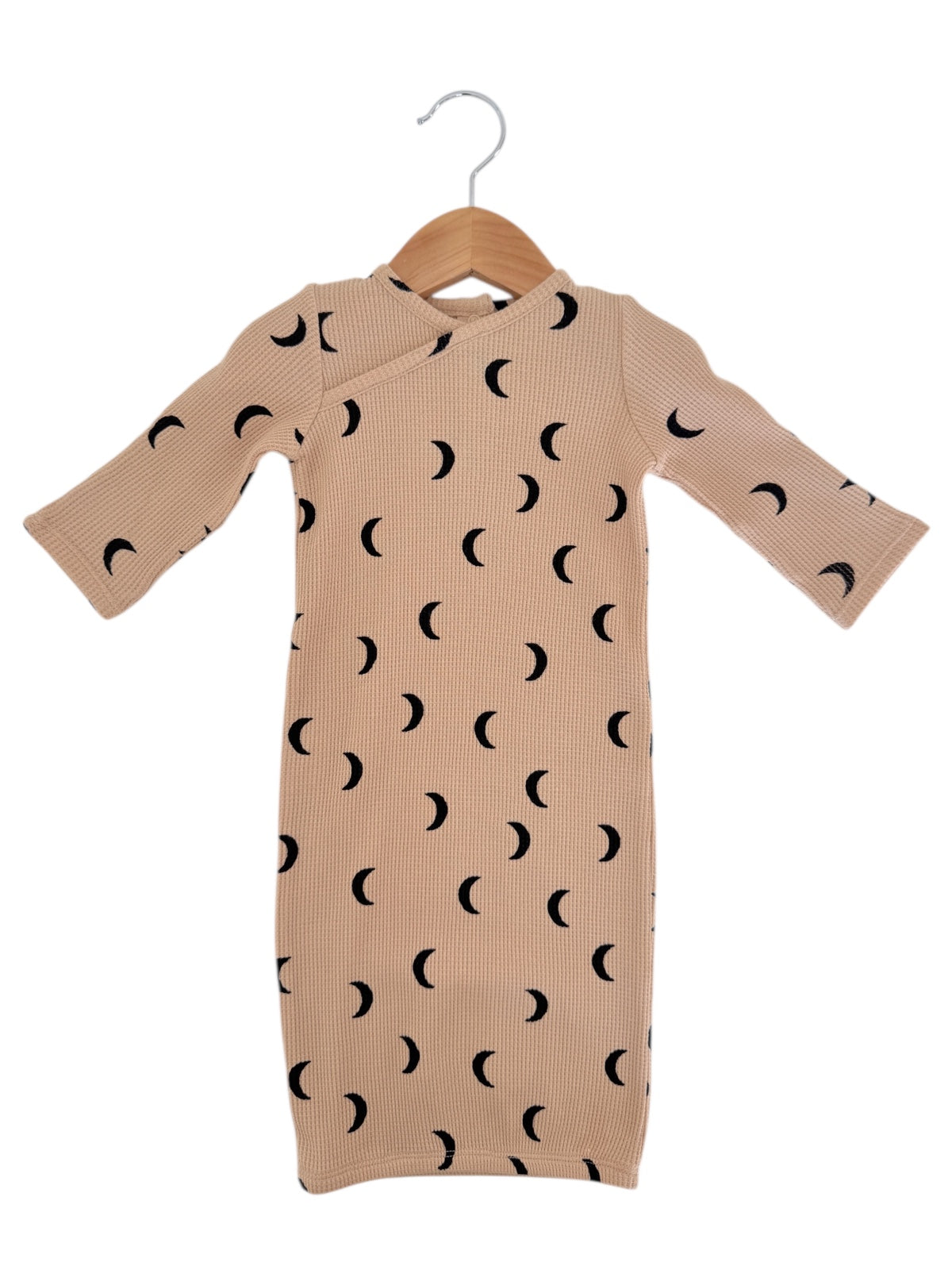 Beige baby dress with black crescent moon pattern hanging on a wooden hanger against a white background.