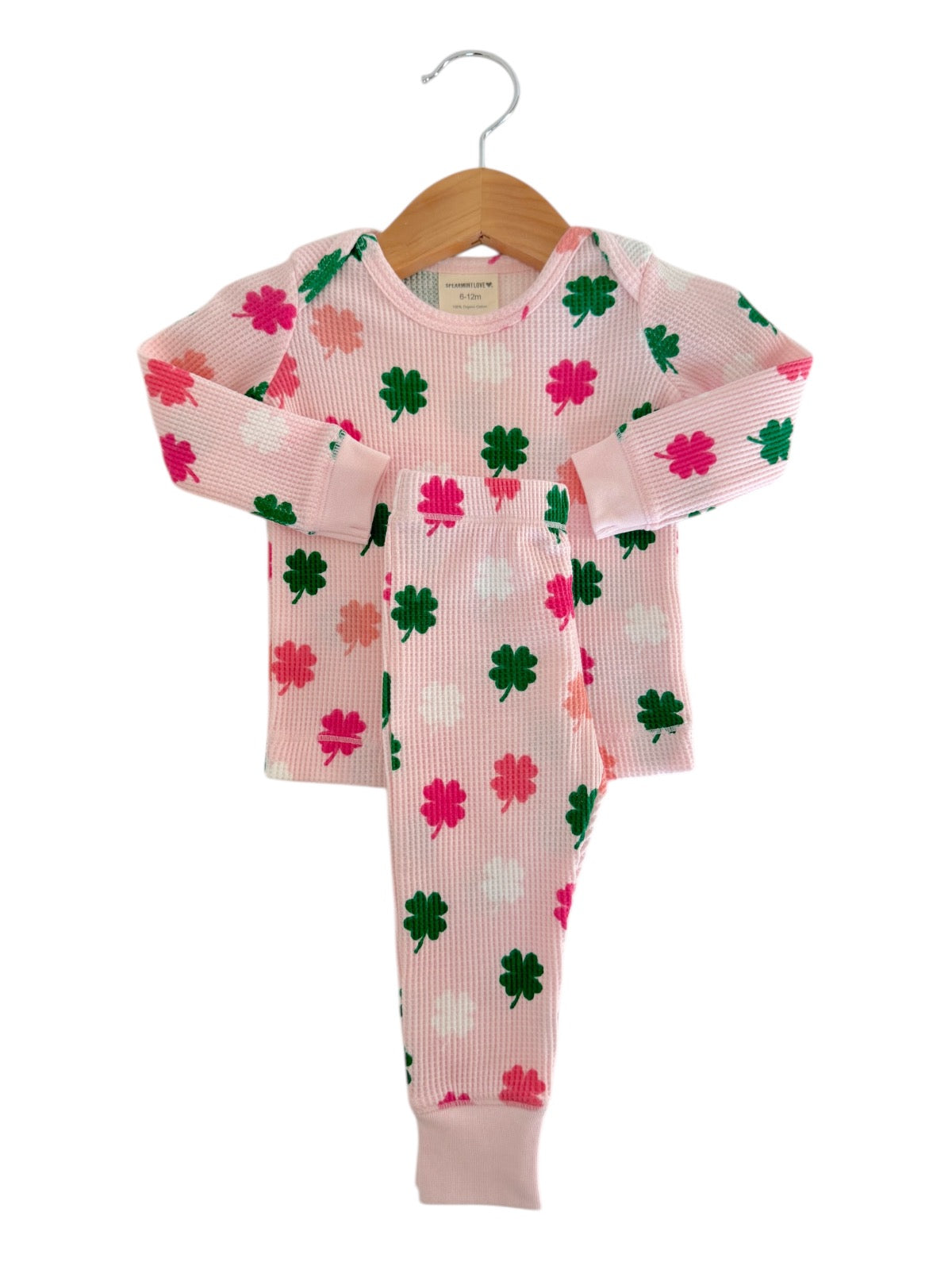 Pink kids' pajamas with colorful clover patterns, hanging on a wooden hanger against a white background.