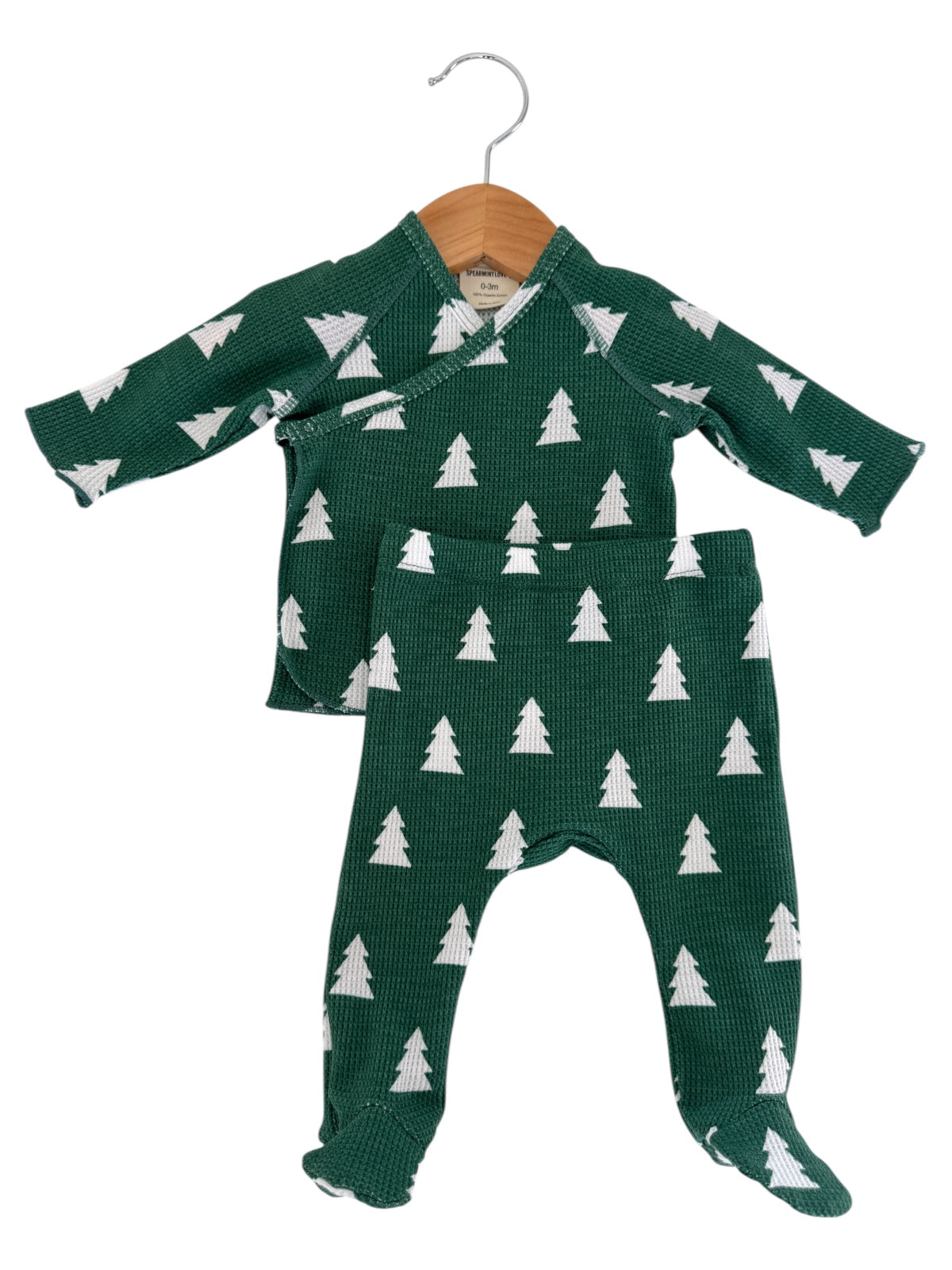 Green baby outfit with white tree patterns, including a top and pants, displayed on a wooden hanger.