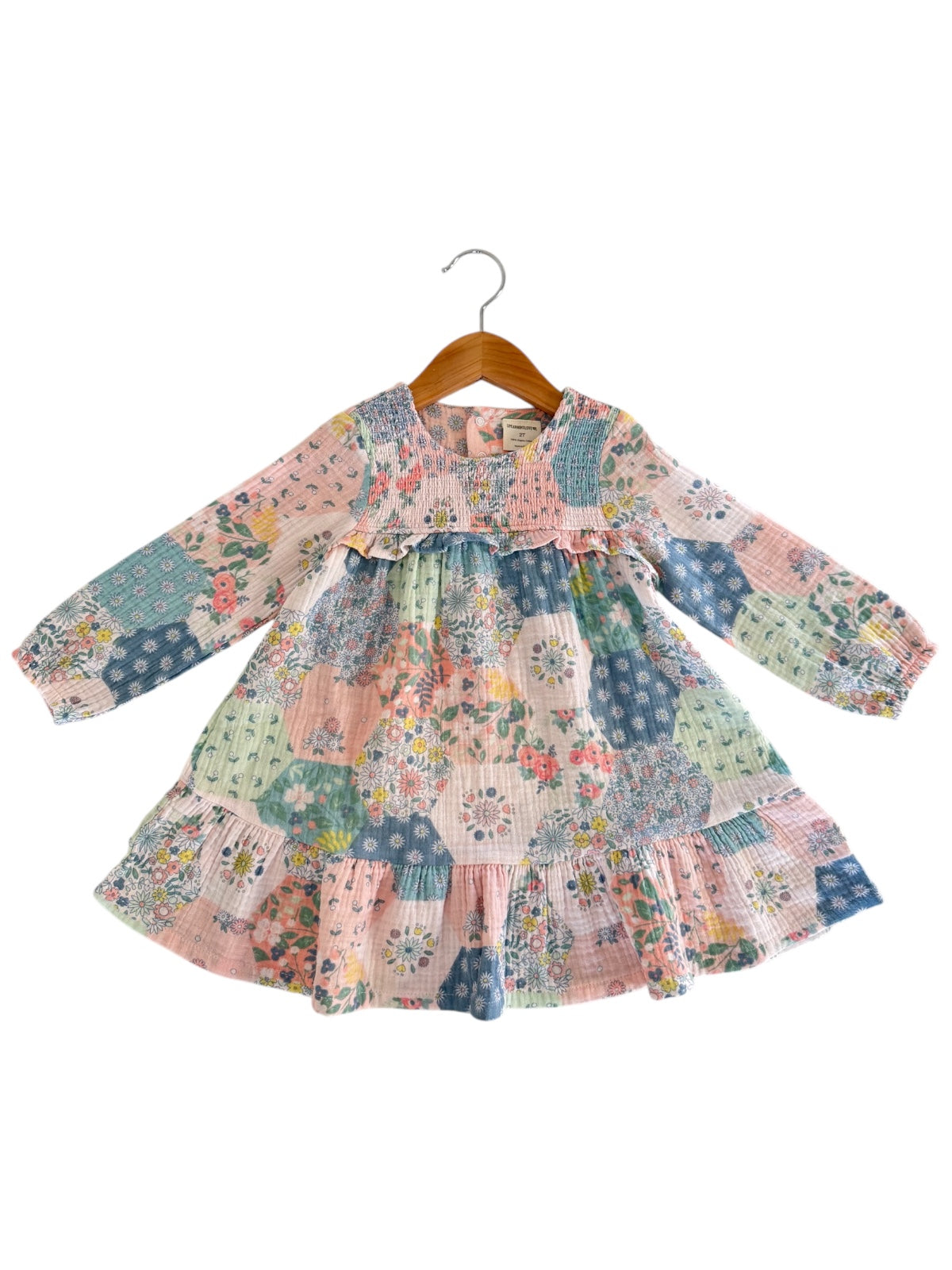 Colorful, patterned girls' dress with long sleeves and ruffle hem, displayed on a wooden hanger.