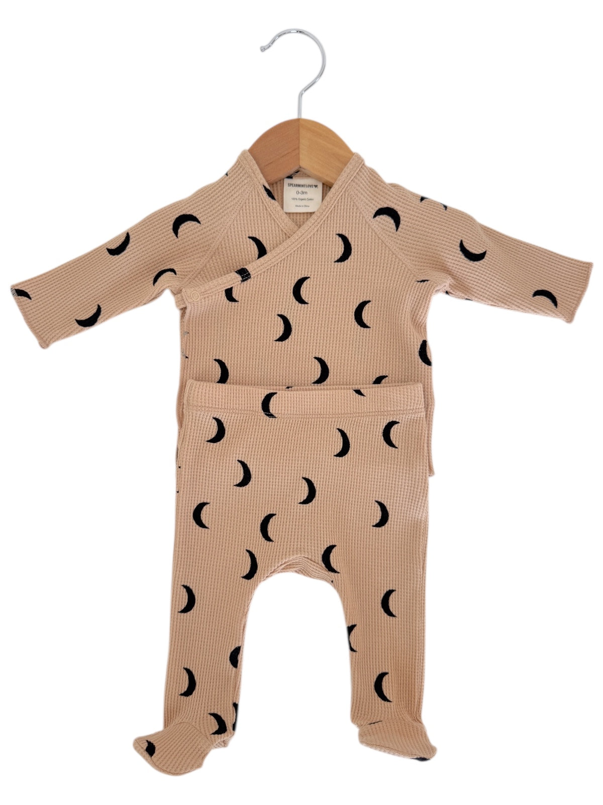 Light brown baby outfit with black crescent moon patterns, hanging on a wooden hanger.